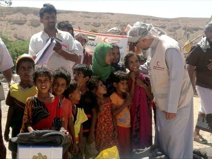 Un miembro de la Media Luna Roja de EAU junto a niños yemeníes.