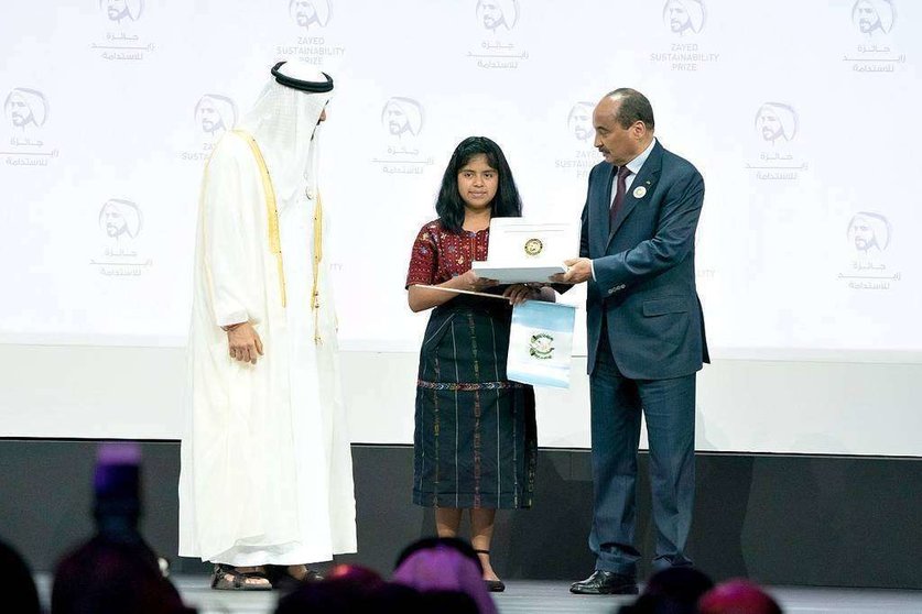 Momento en el que la representante de la escuela Impact de Guatemela, bandera de su país en mano, recibe en Abu Dhabi del jeque Mohammed bin Zayed Al Nahyan el Premio Zayed de Sostenibilidad en la categoría de las Américas. (WAM)