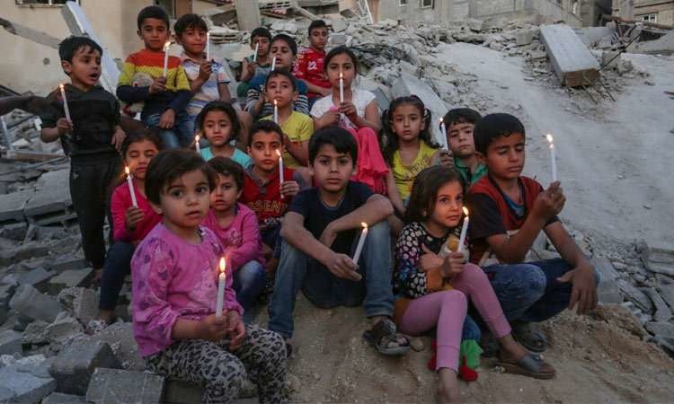 Niños palestinos sostienen velas en las ruinas de un edificio destruido en los recientes ataques aéreos israelíes. (Fuente externa)
