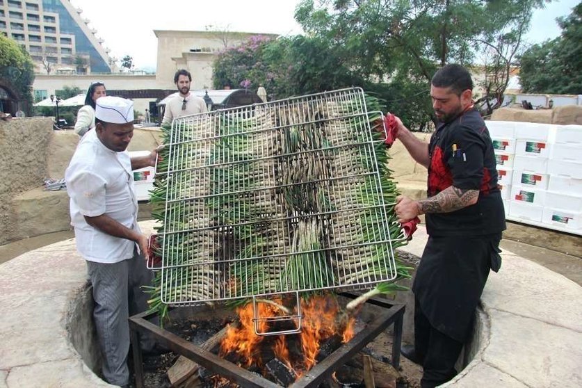 El chef Aleix Font -derecha- dispone sobre el fuego la gran parrilla con los calçots. (EL CORREO)