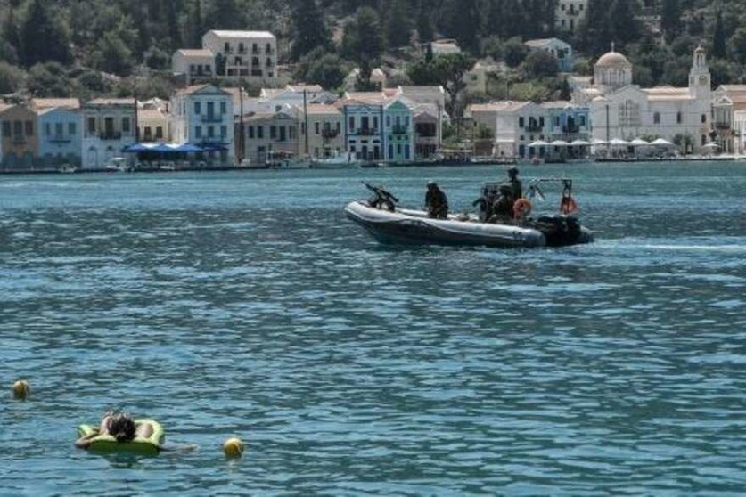Una mujer toma el sol en el mar, mientras que una embarcación militar griega se dirige hacia la isla de Kastelórizo, epicentro de las disputas entre Grecia y Turquía. (AFP)