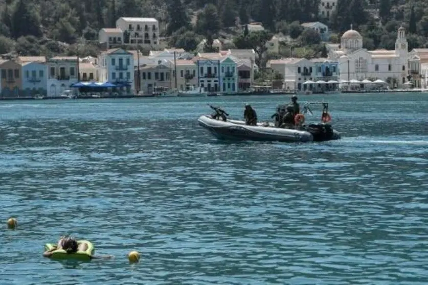 Una mujer toma el sol en el mar, mientras que una embarcación militar griega se dirige hacia la isla de Kastelórizo, epicentro de las disputas entre Grecia y Turquía. (AFP)