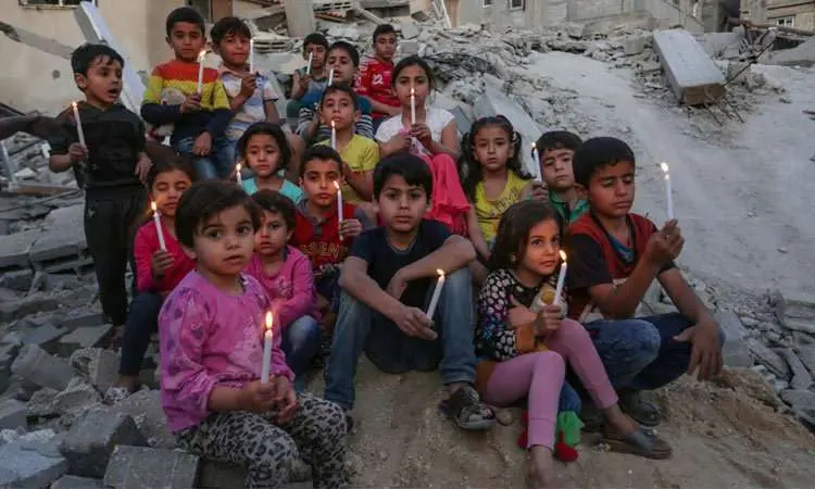 Niños palestinos sostienen velas en las ruinas de un edificio destruido en los recientes ataques aéreos israelíes. (Fuente externa)