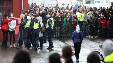 Oficiales de policía suecos brindan información a personas, mientras intentan asegurar el área exterior de la escuela. (AFP)