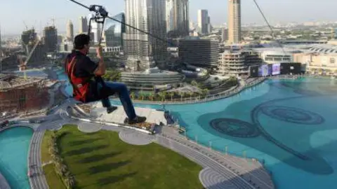 Un deportista se lanza en tirolina por la Fuente de Dubai.