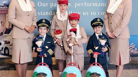 Personal de cabina y niños ataviados con el uniforme de Emirates Airline.