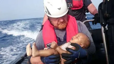 El bebé ahogado en el Mediterráneo es acunado por un voluntario alemán.