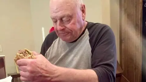 Abuelo come en solitario una hamburguesa.