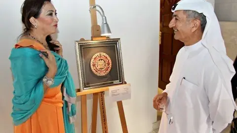 La pintora mexicana Miryam Kruisher-Ortega explica a un ciudadano emiratí el sentido de su obra tridimensional en madera 'The Sun Stone'. (EL CORREO)
