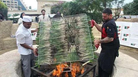 El chef Aleix Font -derecha- dispone sobre el fuego la gran parrilla con los calçots. (EL CORREO)