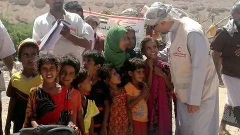 Un miembro de la Media Luna Roja de EAU junto a niños yemeníes.