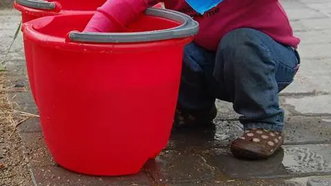 Una niña juega con un cubo de agua.