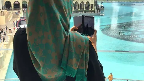 Una mujer musulmana toma imágenes de la fuente situada ante el Burj Khalifa en Dubai. (EL CORREO)