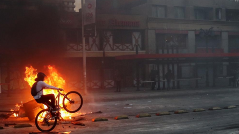 En la imagen de Reuters, un manifestante monta una bicicleta frente a una hoguera improvisada durante una protesta en Santiago de Chile.