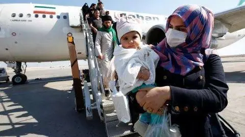 Una madre protegida con mascarilla baja de un avión iraní. (Reuters)