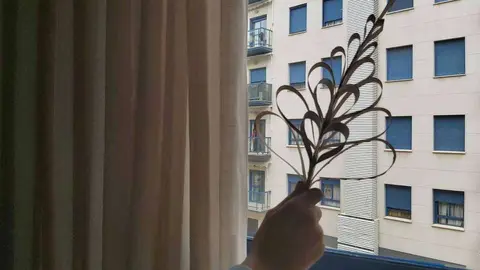 Un niño muestra por la ventana una palma elaborada con cartulina. (EL CORREO)