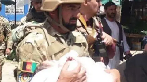 Un miembro de las Fuerzas de Seguridad en Kabul lleva en brazos a un recién nacido. (Twitter)