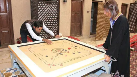 María Tello, directora de Passion Dubai Tours y autora del texto, observa cómo Mohammed Naved, de EL CORREO DEL GOLFO, juega al Carrom en el Centro Cultural para el Entendimiento, situado en el tradicional barrio de Al Fahidi en Dubai. (EL CORREO)