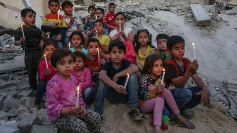 Niños palestinos sostienen velas en las ruinas de un edificio destruido en los recientes ataques aéreos israelíes. (Fuente externa)