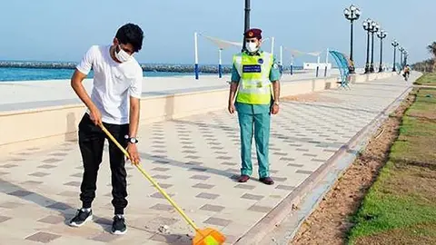 Uno de los condenados limpia una acera bajo la supervisión de un policía. (Gulftoday)