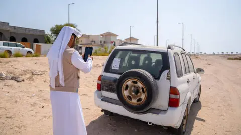Un funcionario fotografía un coche abandonado en el emirato de Abu Dhabi. (WAM)