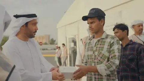 Un funcionario del Ministerio de Recursos Humanos y Emiratización entrega una caja con alimentos a un trabajador. (MoHRE)