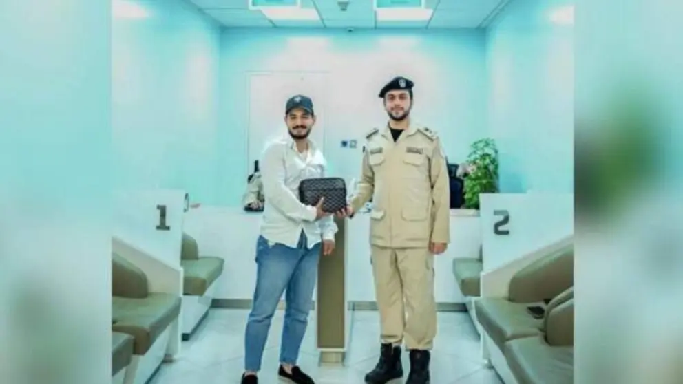 Un agente de la polic&iacute;a de Sharjah entrega la bolsa recuperada a su due&ntilde;o. (Polic&iacute;a de Sharjah)